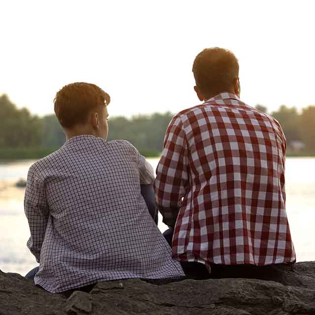 A dad sitting with a teenage son next to a lake.